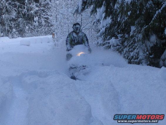 Snowmobile kicking up snow, rider wearing goggles and camouflage jacket