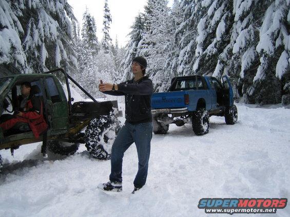 Two modified off-road vehicles parked in a snow-covered forest with a man standing between them