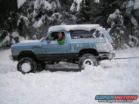 Light blue Dodge Ramcharger stuck in deep snow, driver visible