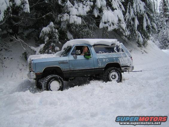 Light blue SUV with snow on roof stuck in deep snow, driver visible