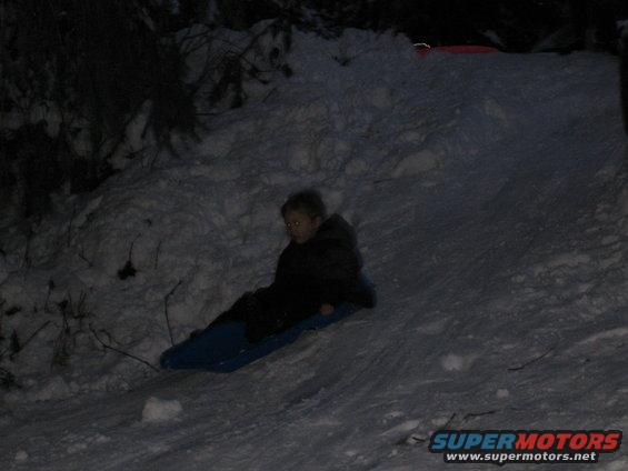 Child on a blue sled going down a snow-covered slope at night