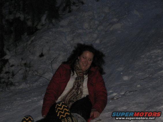Woman in red jacket and scarf sledding down a snowy hill at night