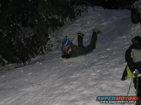 Two people sledding down a snowy hill at night