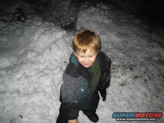 Child in a snow-covered area, wearing a jacket and green shirt