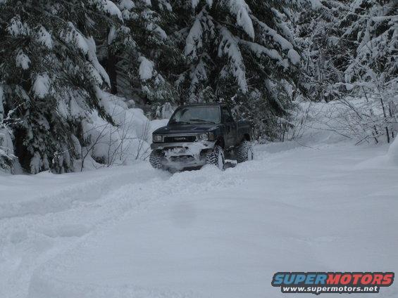 Dark Toyota pickup truck with large tires driving through deep snow