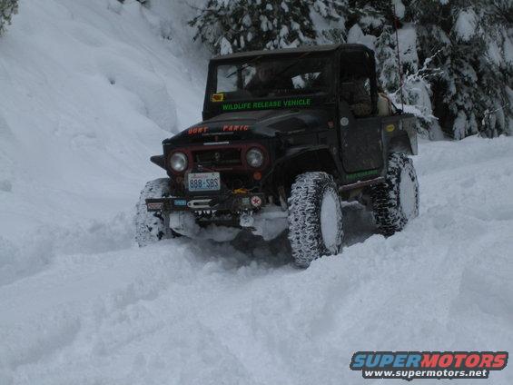 Black off-road vehicle with large tires driving through deep snow, green text on windshield reads 'WILDLIFE RELEASE VEHICLE'