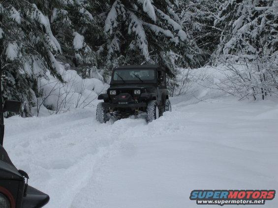 Black Jeep Wrangler driving through snow-covered forest road
