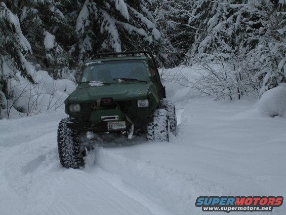Green 1990 Ford Bronco driving through deep snow