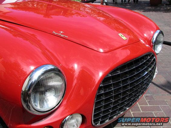 Red vintage car front with chrome grille and headlights, 'Superleggera' script on hood