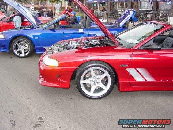 Red convertible sports car with hood open, showing silver five-spoke wheels and side racing stripes