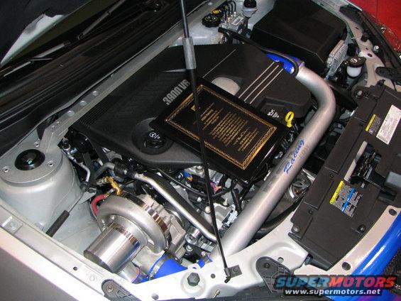 Engine bay with a turbocharger, intake piping, and a plaque on the engine cover
