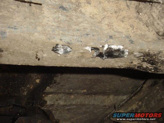 Undercarriage of a vehicle with white and black paint marks on a metal beam