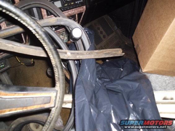 Close-up of a vehicle's interior, showing a steering wheel, dashboard, and a black trash bag. A cardboard box is visible on the right
