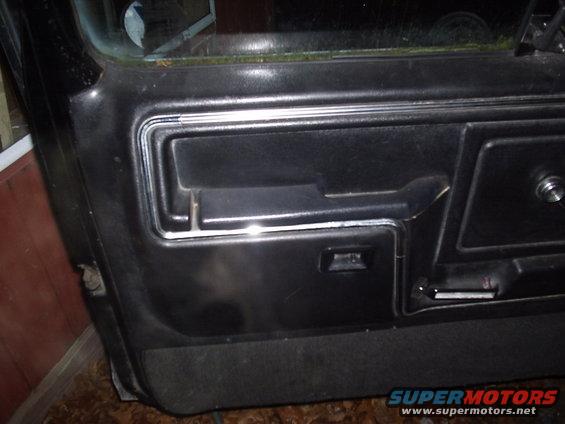 Black car door panel with chrome trim and a pull handle. Visible text: www.supermotors.net