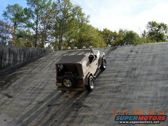 Tan Jeep Wrangler with soft top and spare tire on rear climbing a steep concrete incline