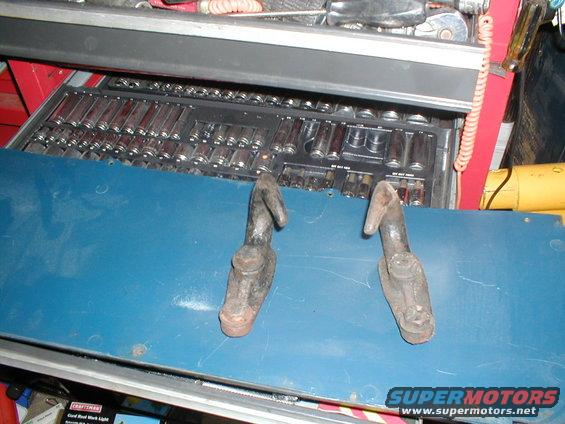 Two old tow hooks resting on a blue surface above a toolbox filled with sockets