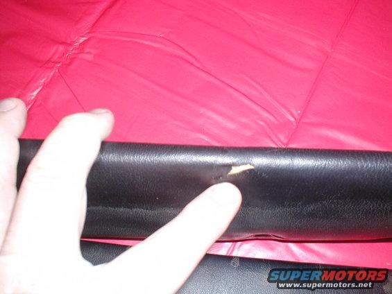 Black leather trim with a small tear, a finger pointing at the damage