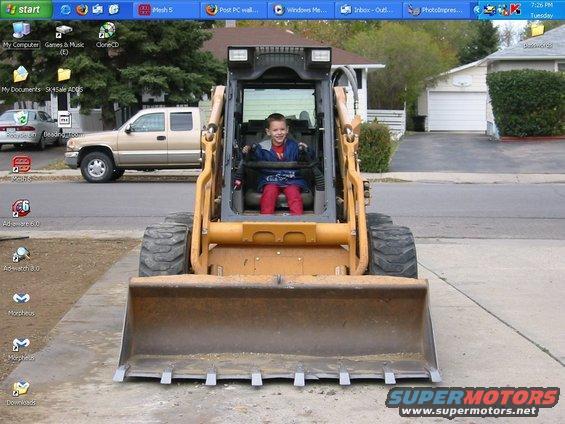 Child sits in the driver's seat of a yellow skid steer loader with a large bucket