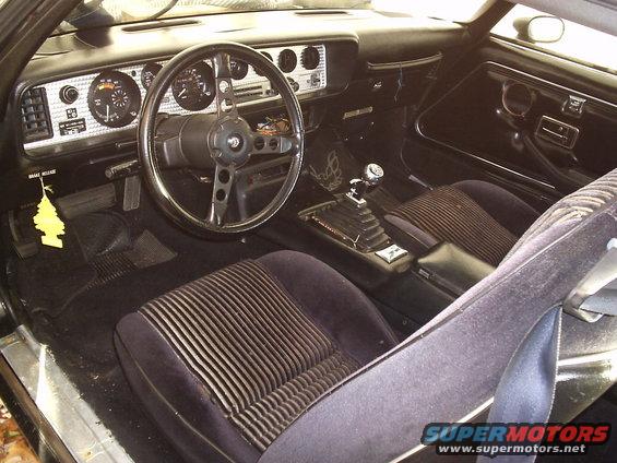 Car interior with striped cloth seats, dashboard, steering wheel, and floor shifter