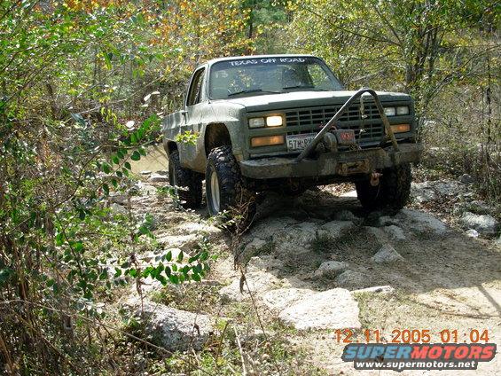 Green pickup truck with winch driving over rocks on a trail. Has 'TEXAS OFF ROAD' sticker on windshield