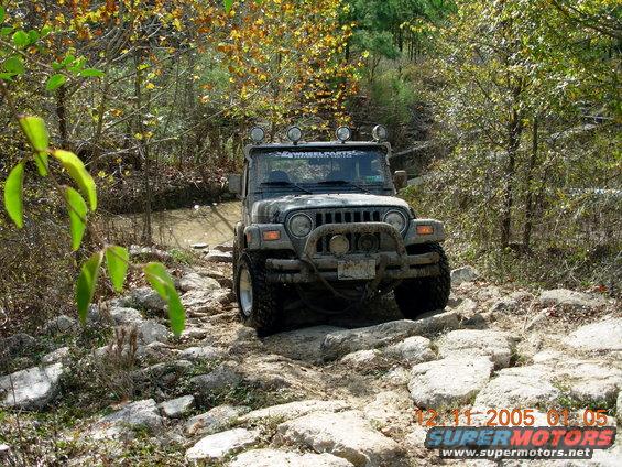 Mud-covered Jeep Wrangler on a rocky trail, front view