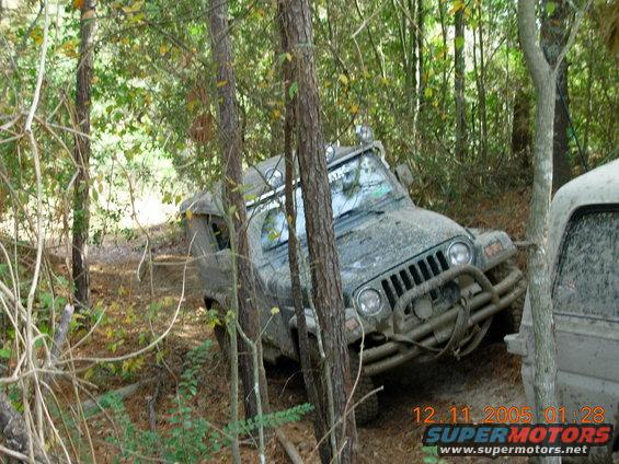 Muddy Jeep Wrangler on wooded trail, another vehicle partially visible