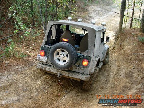 Jeep Wrangler TJ with soft top on a muddy trail, rear view. License plate W41-ZMC