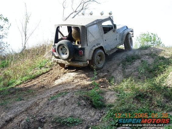 Muddy Jeep Wrangler climbing a dirt hill, spare tire on back