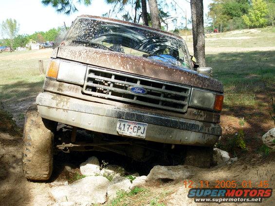 Brown 1987 Ford Bronco, mud-splattered, tilted on rocks, front view