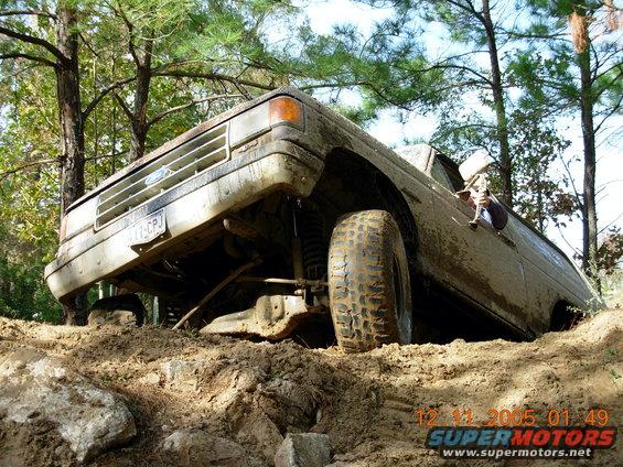 Mud-covered 1980s Ford Bronco tilted on a dirt trail with visible suspension and tires