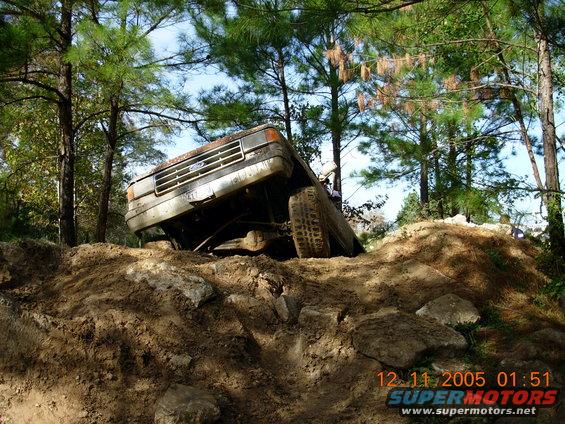 1987 Ford Bronco tilted on a dirt hill with trees in background