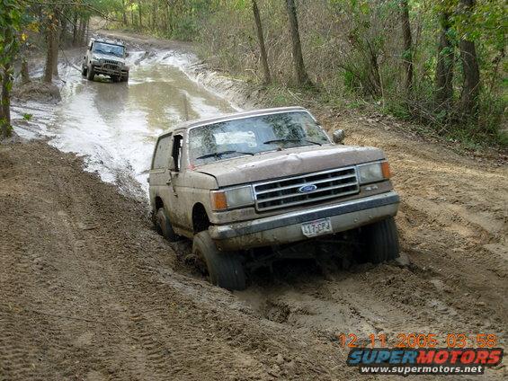 Brown 1987 Ford Bronco stuck in mud on a trail, front grille visible