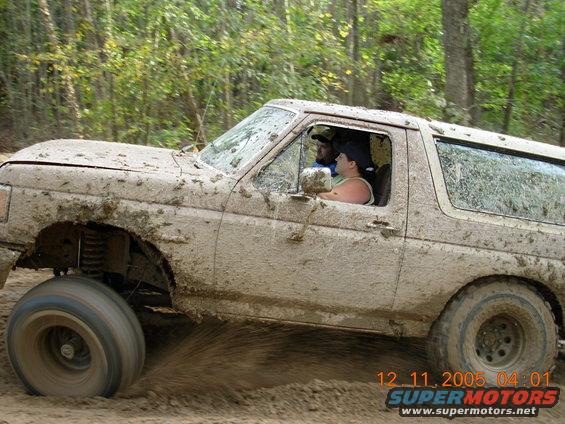Mud-covered 1987 Ford Bronco driving off-road, side view