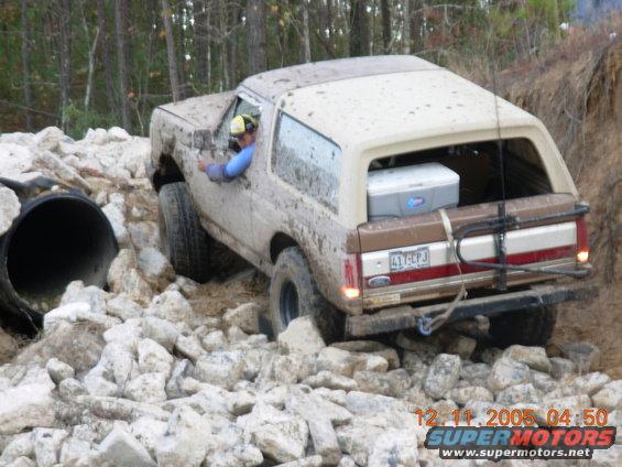 1987 Ford Bronco navigating a rocky, off-road obstacle course with a large pipe