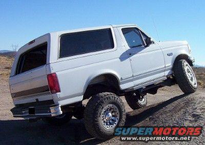 White 1995 Ford Bronco on a dirt incline, rear-left quarter view, lifted suspension, aftermarket wheels