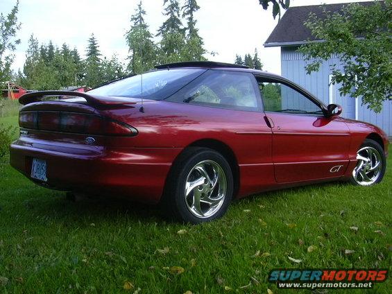 Red 1997 Ford Probe GT coupe with a rear spoiler and chrome wheels parked on grass