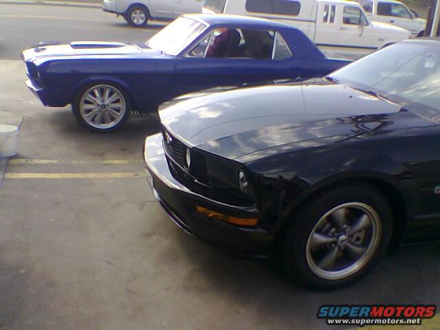 Black 2005 Ford Mustang front quarter panel and wheel, blue classic Mustang behind it