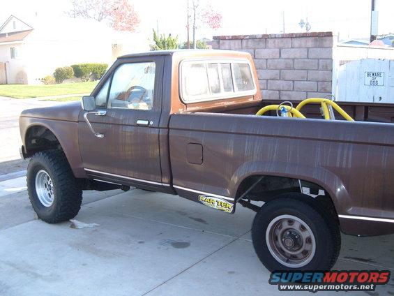 Brown pickup truck with a brown camper shell, lifted suspension, and a yellow roll cage visible in the bed