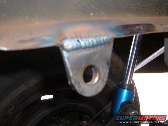 Welded bracket on vehicle frame near tire and blue shock absorber