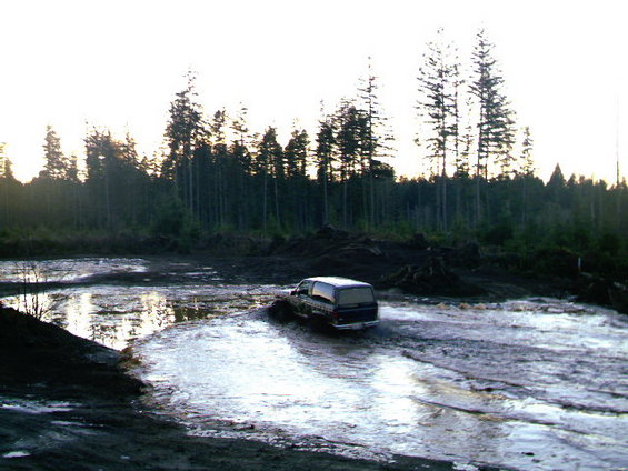 van driving through a muddy, watery area with trees in the background