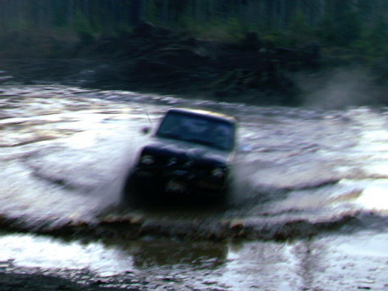 Dark SUV driving through murky water, front view. Appears to be from the 1980s