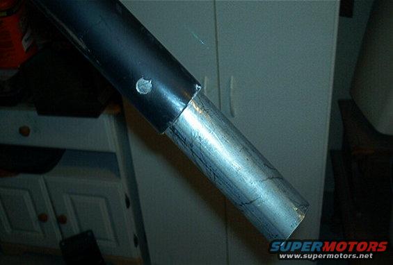 Black and silver metal tubing joined together, with a visible bolt. Background shows cabinets