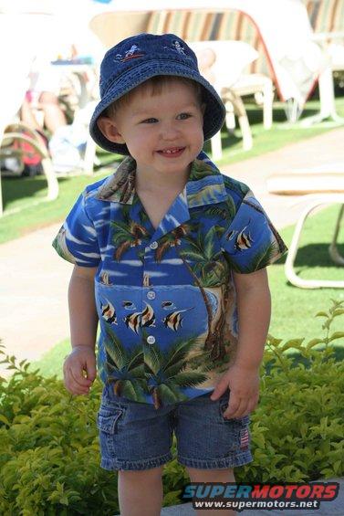 Child in blue Hawaiian shirt with fish and palm trees, denim shorts, and a blue bucket hat