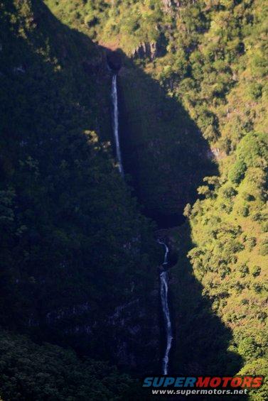 Waterfalls cascade down a lush, green mountainside, casting a shadow