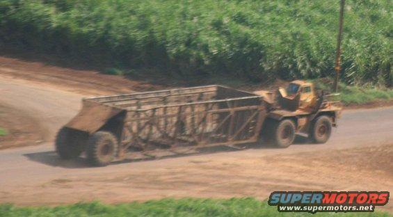 Yellow truck cab pulling a large agricultural trailer on a dirt road