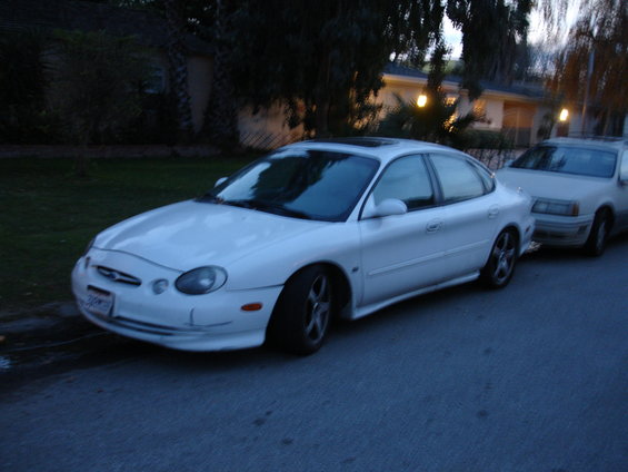 White sedan parked on street, front 3/4 view, slight damage on front bumper