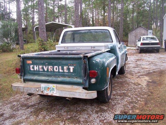 Green 1974 Chevrolet C/K Pickup truck parked outdoors, rear view. Another car is visible in the background