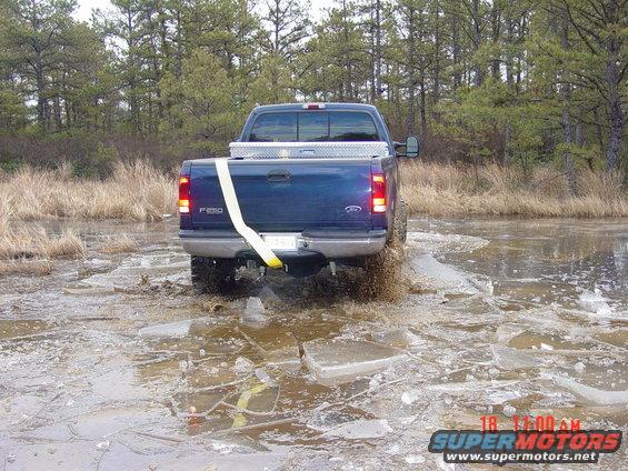 Blue Ford F-250 driving through ice and water, rear view