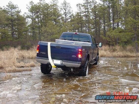 Blue Ford F-250 pickup truck driving on ice with a yellow strap around the bed