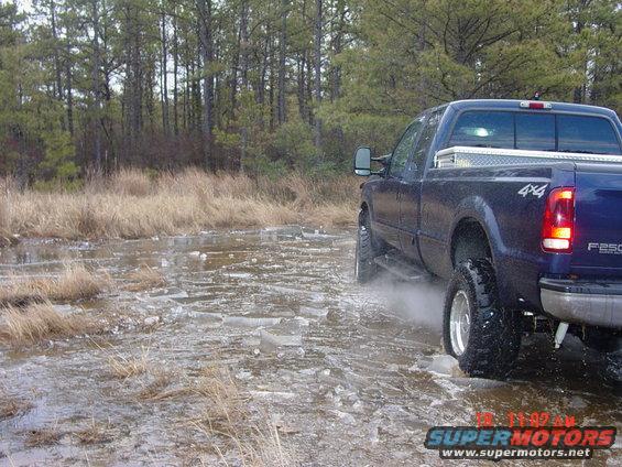 Blue pickup truck with 4x4 badge driving through icy water